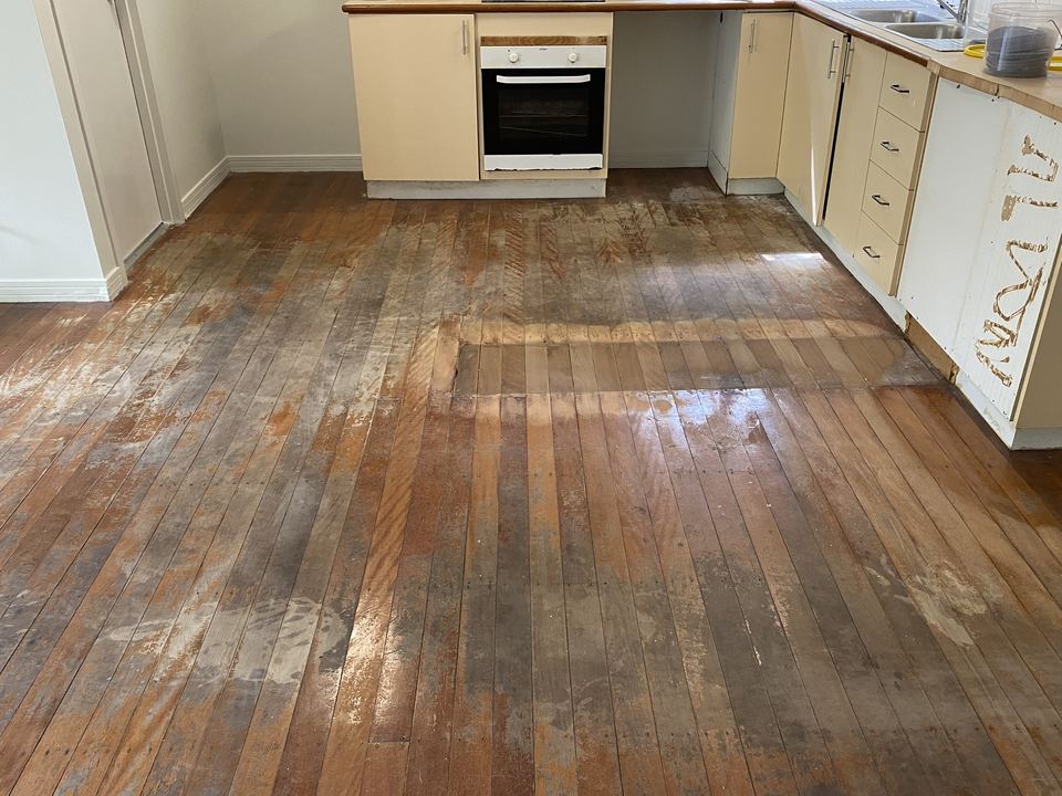 Kitchen floor before sanding, with weathered, patchy grey and brown timber boards.