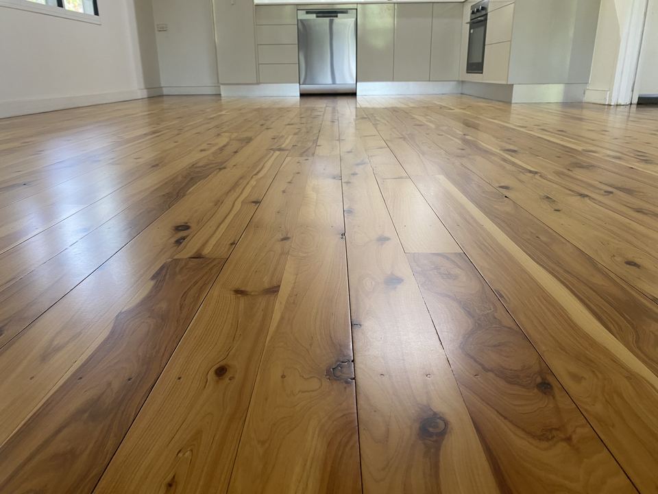 Freshly polished pine floor stretching towards a white kitchen.